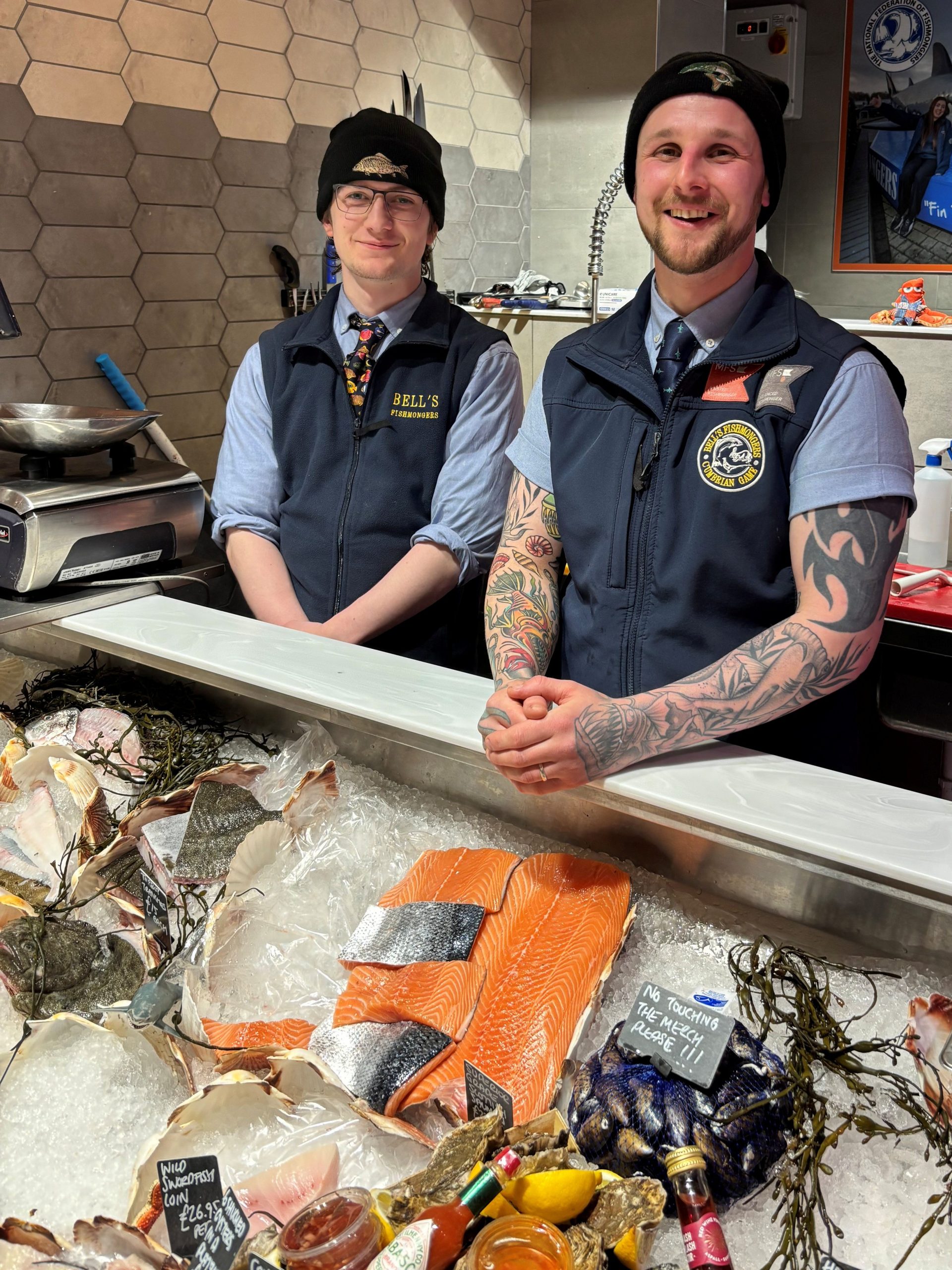 Two fishmongers stood behind a fish counter.